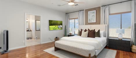 Un dormitorio con cama, ventilador de techo, televisor y ventana con cortinas.