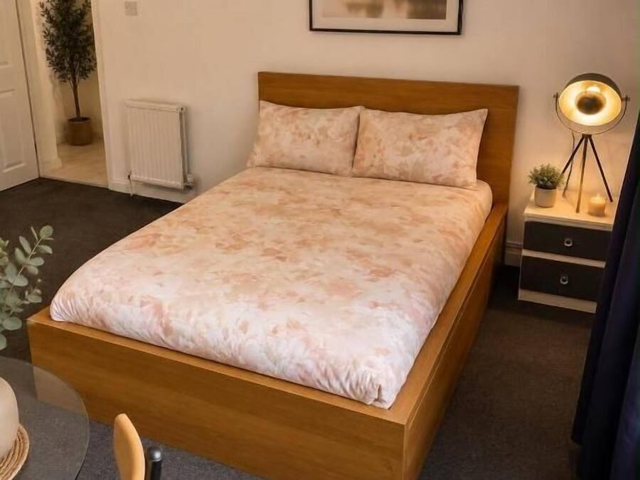 Une chambre avec un lit en bois, une table de chevet avec une lampe, un tableau encadré au mur et une plante en pot.