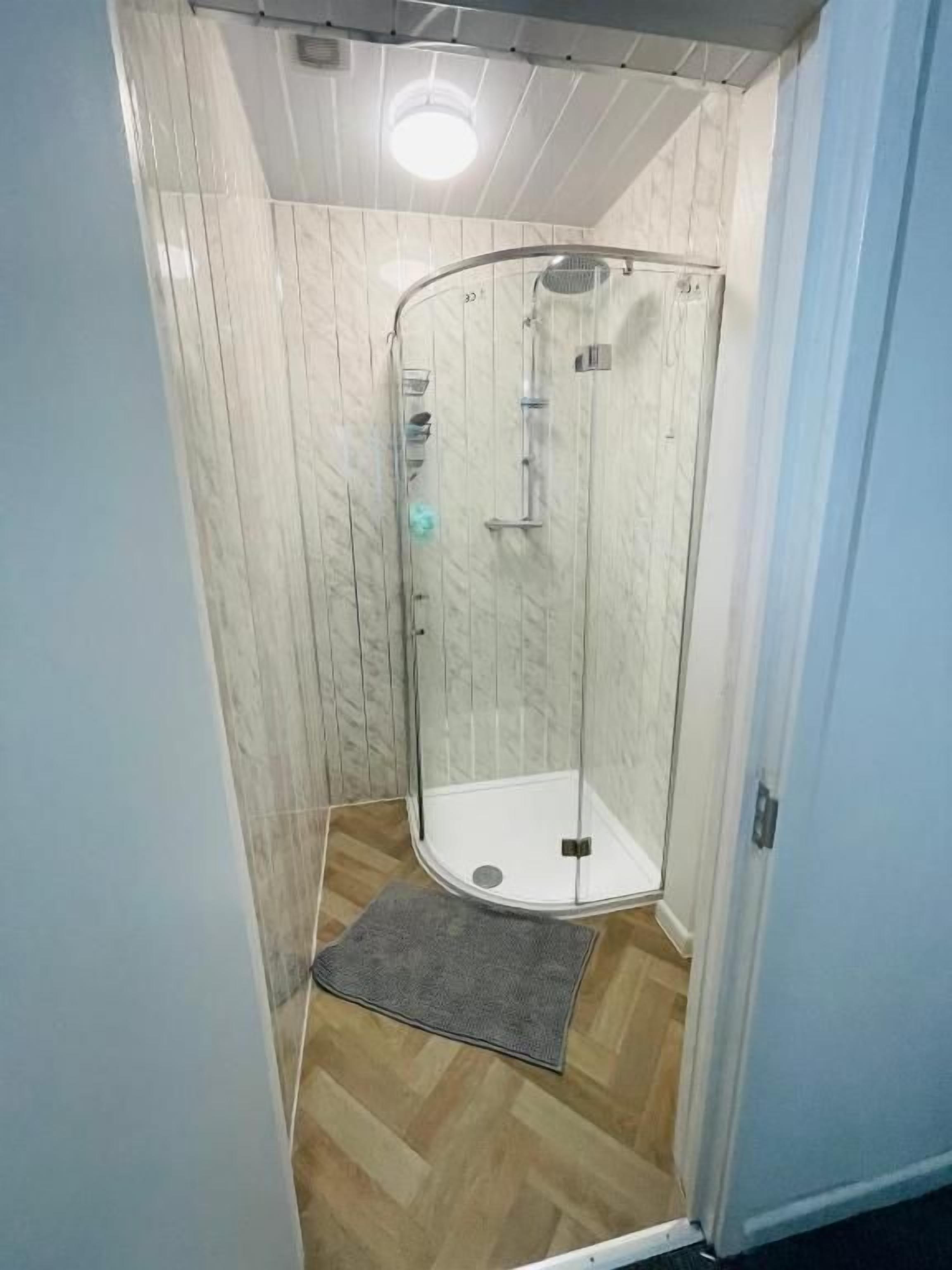 Un petit espace douche fermé, doté d’une porte en verre, d’un pommeau de douche et d’un flexible de douche.