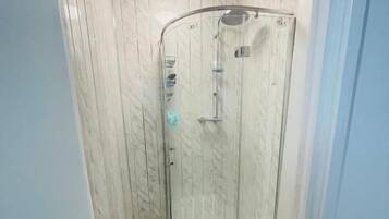 A small, enclosed shower area with a glass door, a showerhead, and a handheld shower attachment.