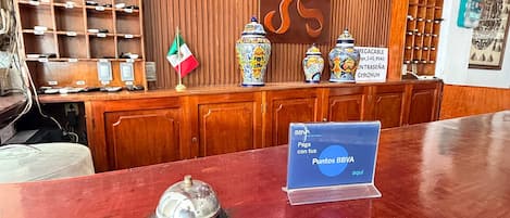 A reception desk with a sign for BBVA points, a flag, and decorative vases.