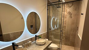 Ein modernes Badezimmer mit einem großen Spiegel, zwei Waschbecken mit runden Schalen, einer Toilette und einer Duschkabine aus Glas.