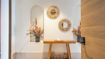 Uma área de recepção com um aparador de madeira, dois espelhos fixados na parede e arranjos florais decorativos.