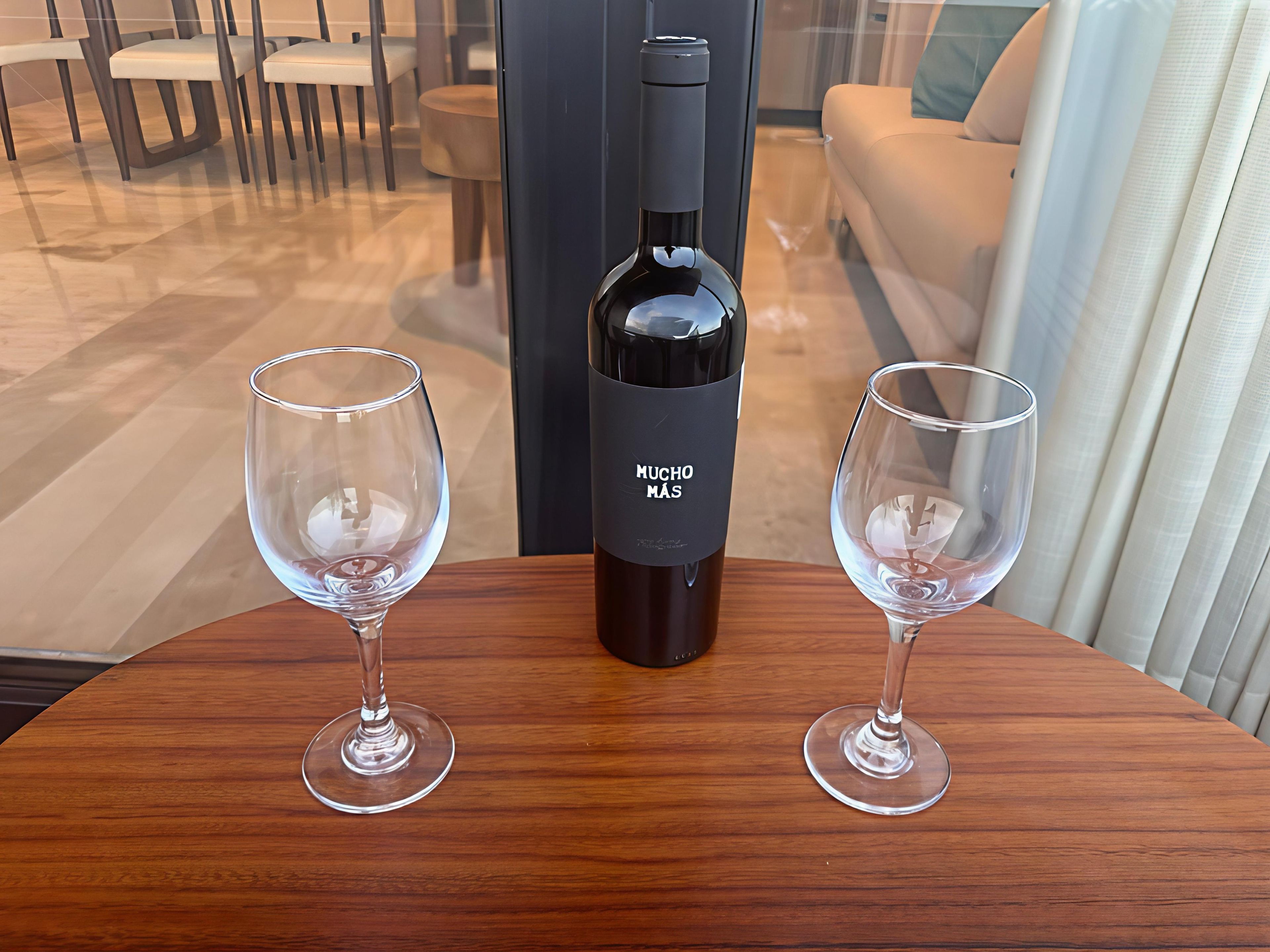 A bottle of wine and two glasses on a wooden table in a room with a sofa and chairs.