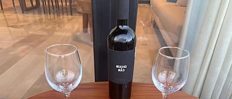 A bottle of wine and two glasses on a wooden table in a room with a sofa and chairs.