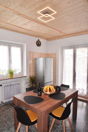 Ein Essbereich mit Holztisch, Stühlen, einem Kühlschrank und einer Zimmerpflanze.