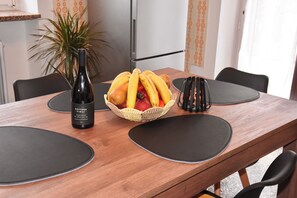 A wooden dining table with a bottle of wine, a basket of fruit, and black placemats. - Terrific 2-bedroom apartment with AC in Trentino-Alto Adige (Trentino-Alto Adige)