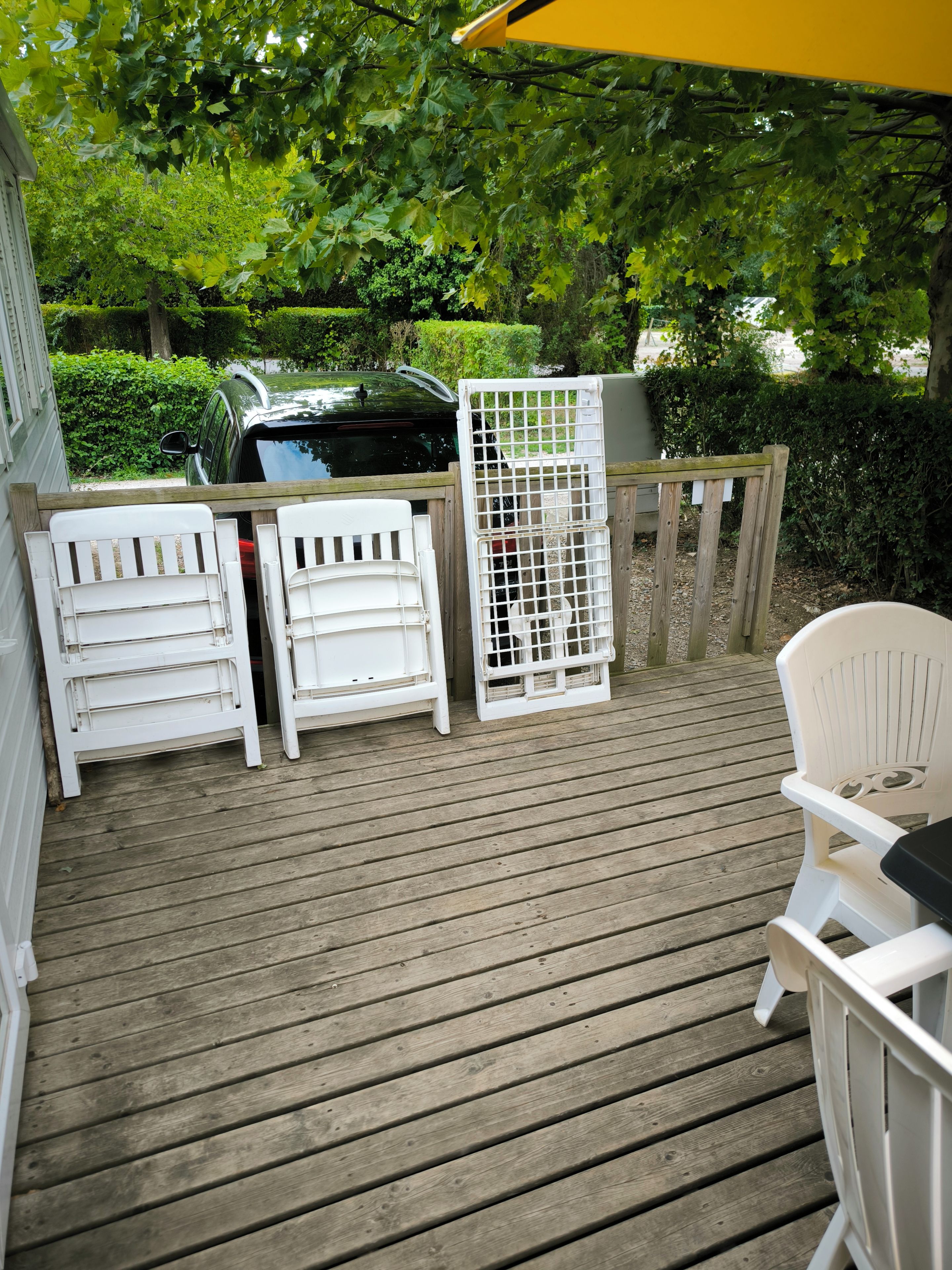 A wooden deck with white outdoor furniture, including chairs and a table, under a yellow umbrella.