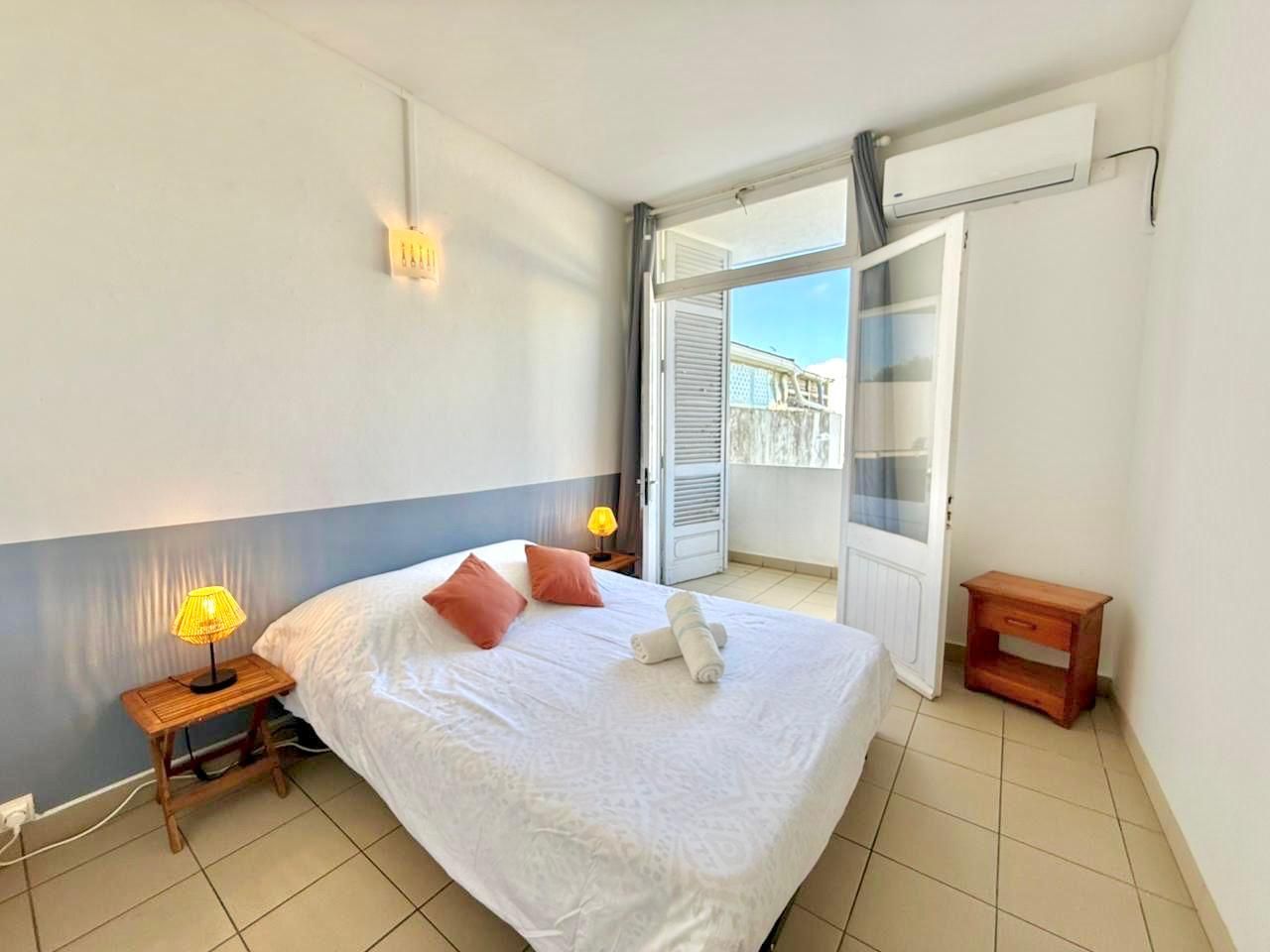 Un dormitorio con cama, lámparas de noche, una mesita de noche de madera y un balcón con puerta corredera.