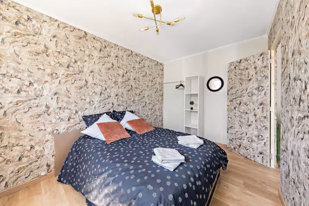 A bedroom with a bed, a round mirror, a white shelf, and a ceiling light fixture.