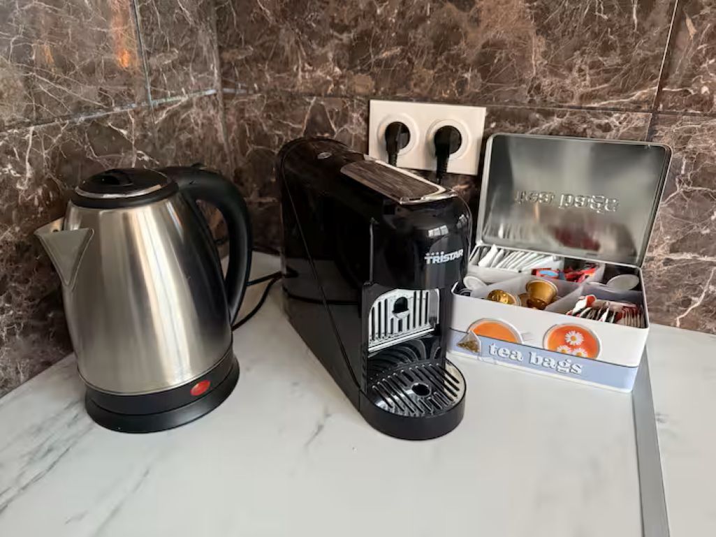 A kitchen counter with a stainless steel kettle, a black coffee maker, and a box of tea bags.