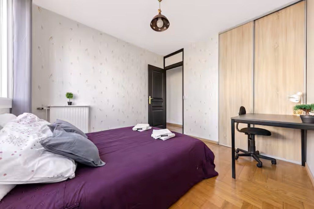 A bedroom with a bed, a desk, and a wardrobe.