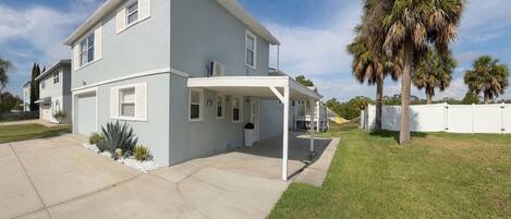 A two-story house with a covered porch, a well-maintained lawn, and a palm tree.