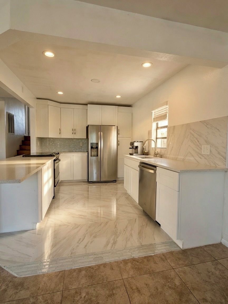 A modern kitchen with white cabinetry, a stainless steel refrigerator, and a marble floor.