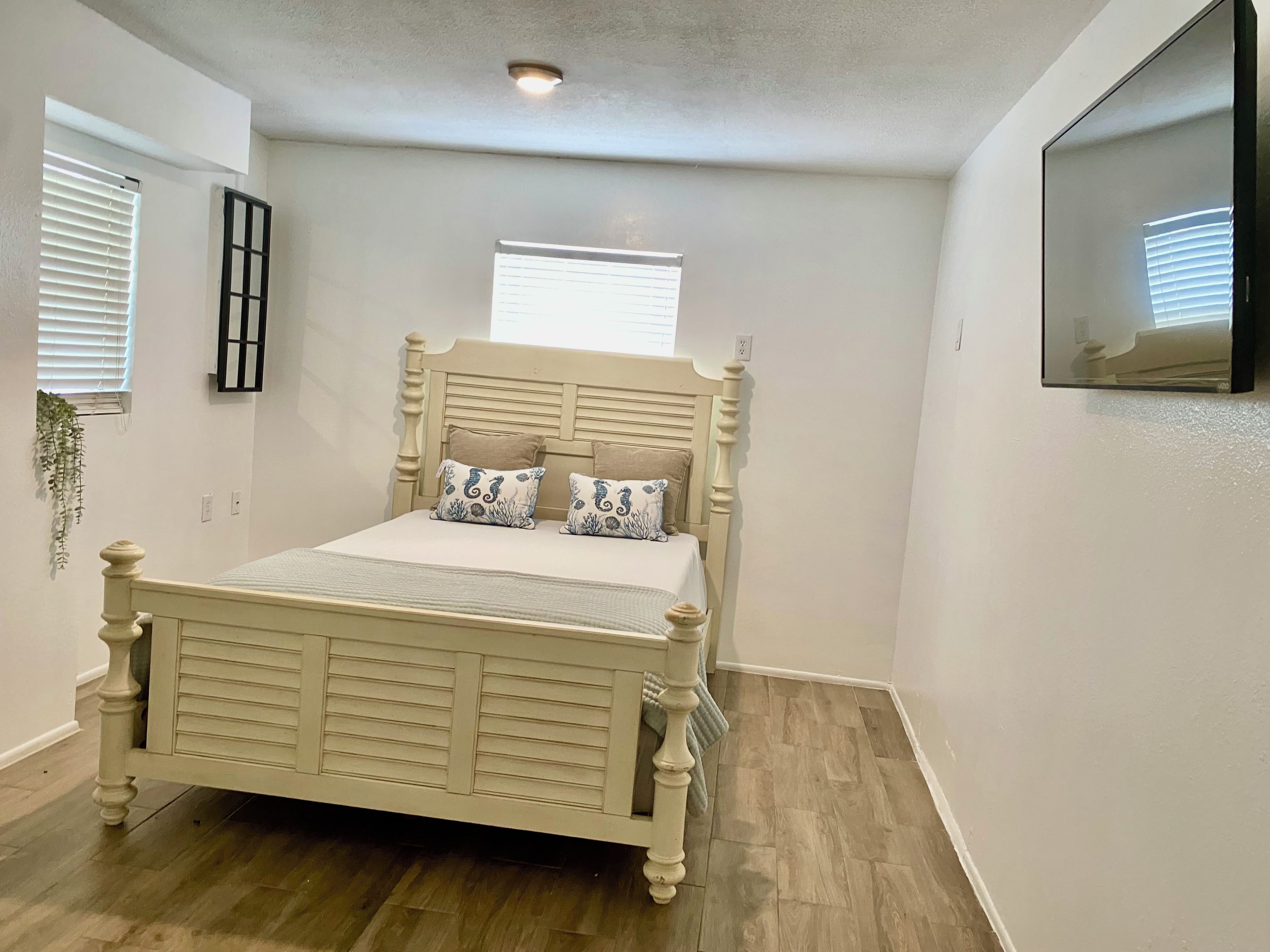 A bedroom with a bed, a window, a wall-mounted TV, and a ceiling light.
