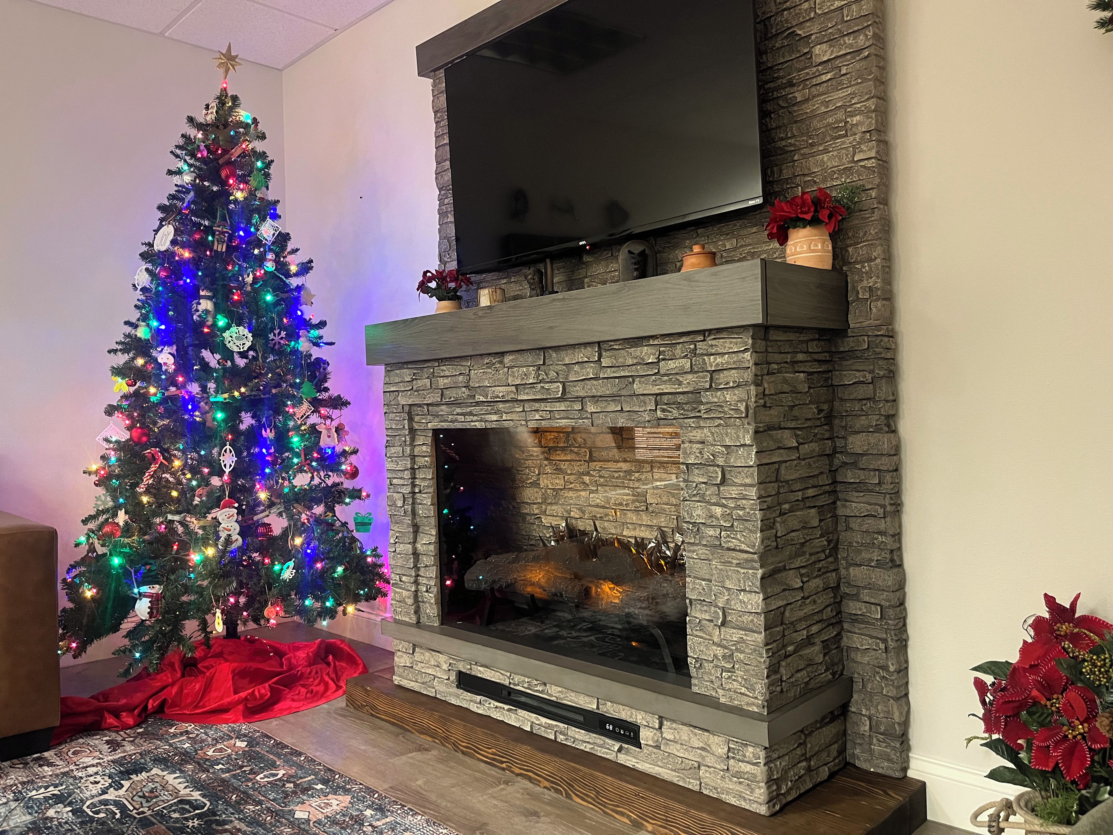 Una sala de estar con chimenea, un árbol de Navidad y un televisor de pantalla plana montado sobre la chimenea.