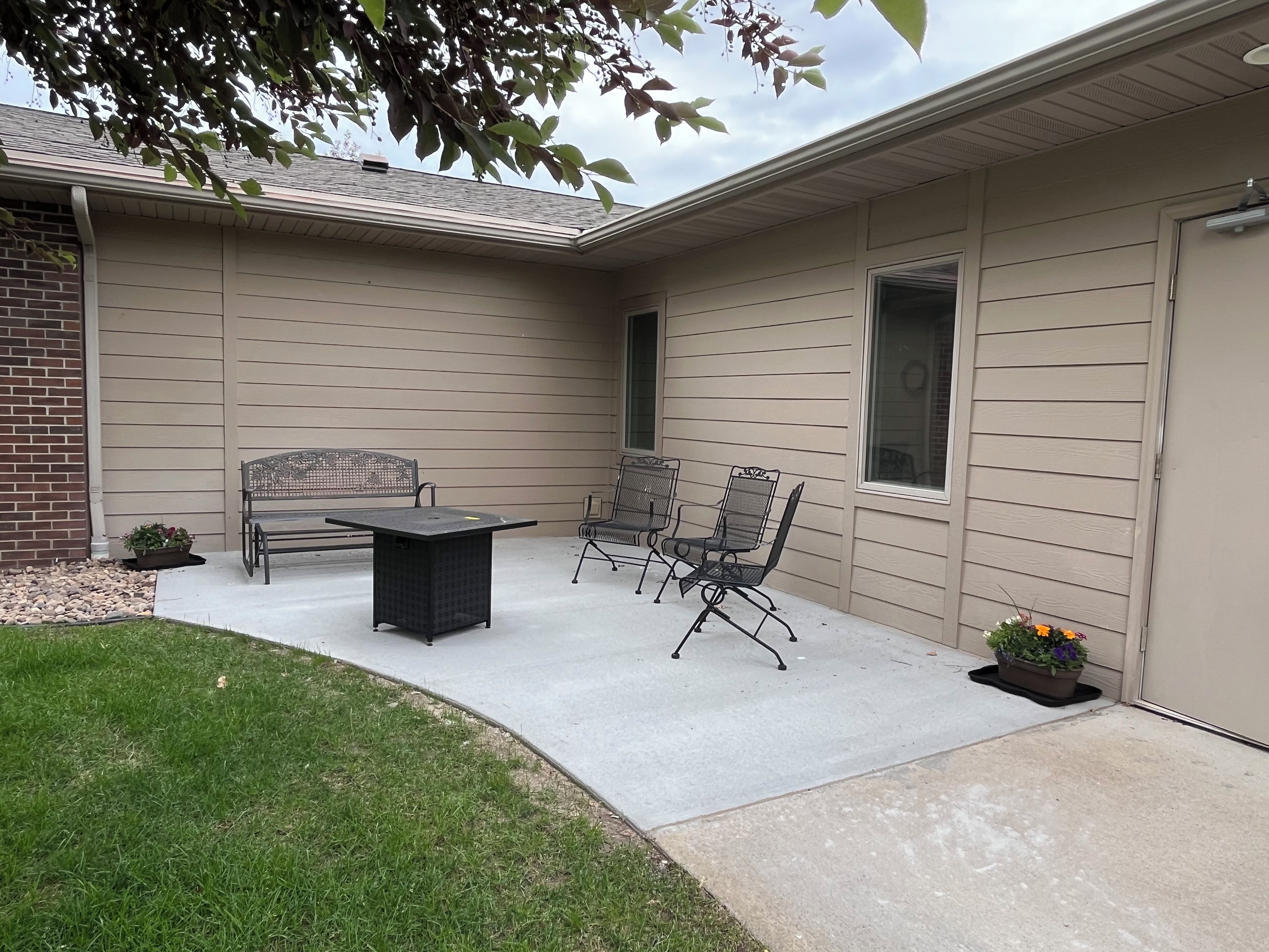 Une terrasse avec une table et des chaises, un petit jardin et un bâtiment doté d’une porte de garage.