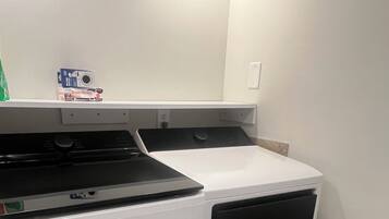 A compact laundry room with a washer and dryer, a small shelf with items, and a tiled floor.