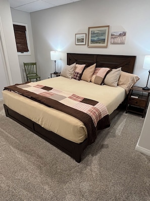 Ein Schlafzimmer mit einem großen Bett, zwei Nachttischen, einem Sessel und gerahmten Bildern an der Wand.