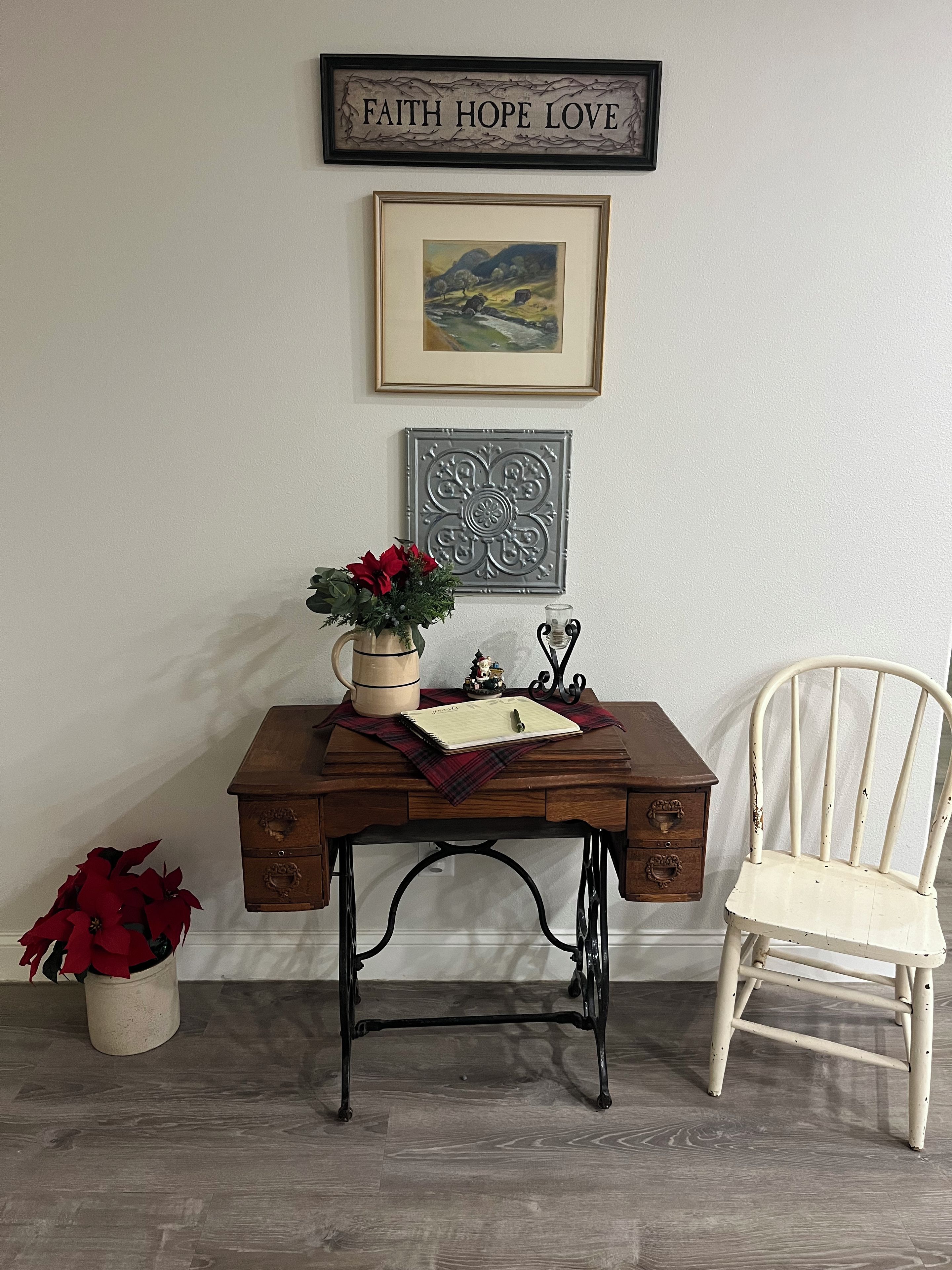 Escritorio de madera con un jarrón de flores rojas, un cuadro enmarcado y un adorno metálico en la pared.