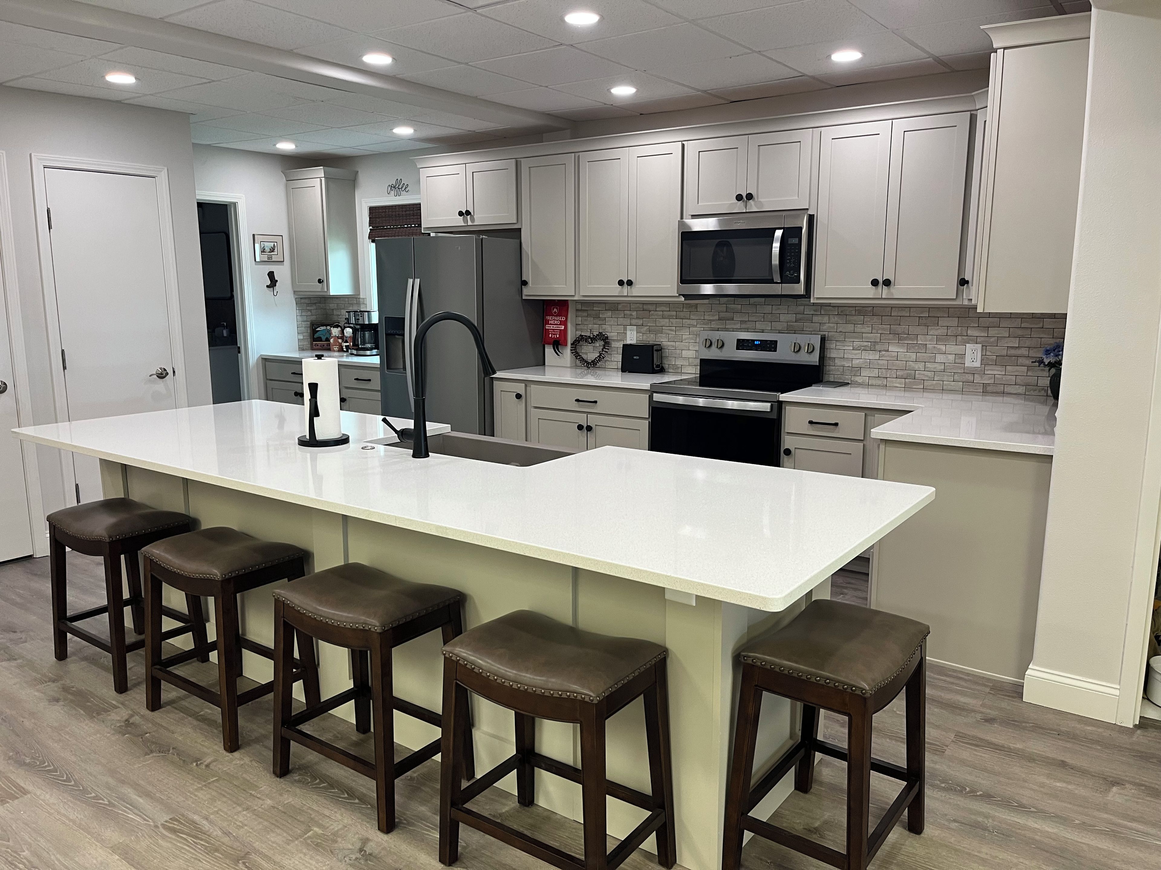 A modern kitchen with a large island, bar stools, stainless steel appliances, and white cabinetry.