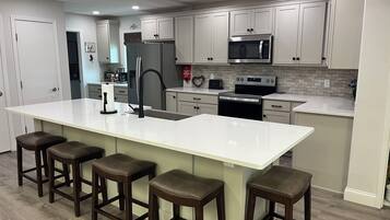 A modern kitchen with a large island, bar stools, stainless steel appliances, and white cabinetry.