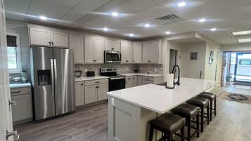 A modern kitchen with stainless steel appliances, a central island with bar stools, and a view of the outside.