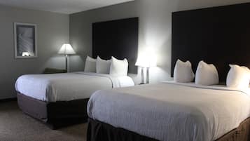 A hotel room with two beds, a large dark headboard, a framed picture on the wall, and a lamp on each side of the beds.