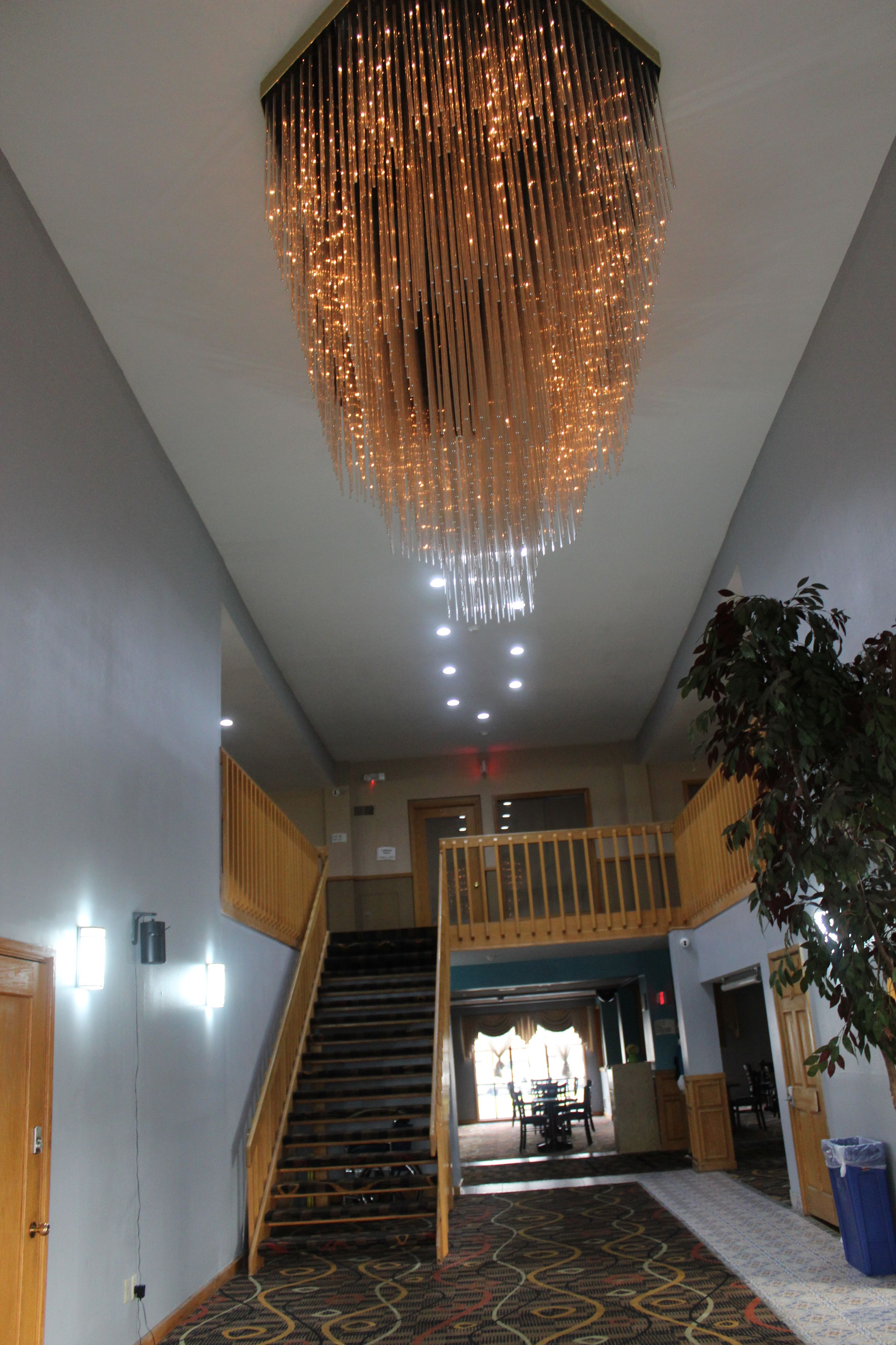 A staircase leading to a second floor with a patterned carpet, a hanging light fixture, and a plant in the foreground.