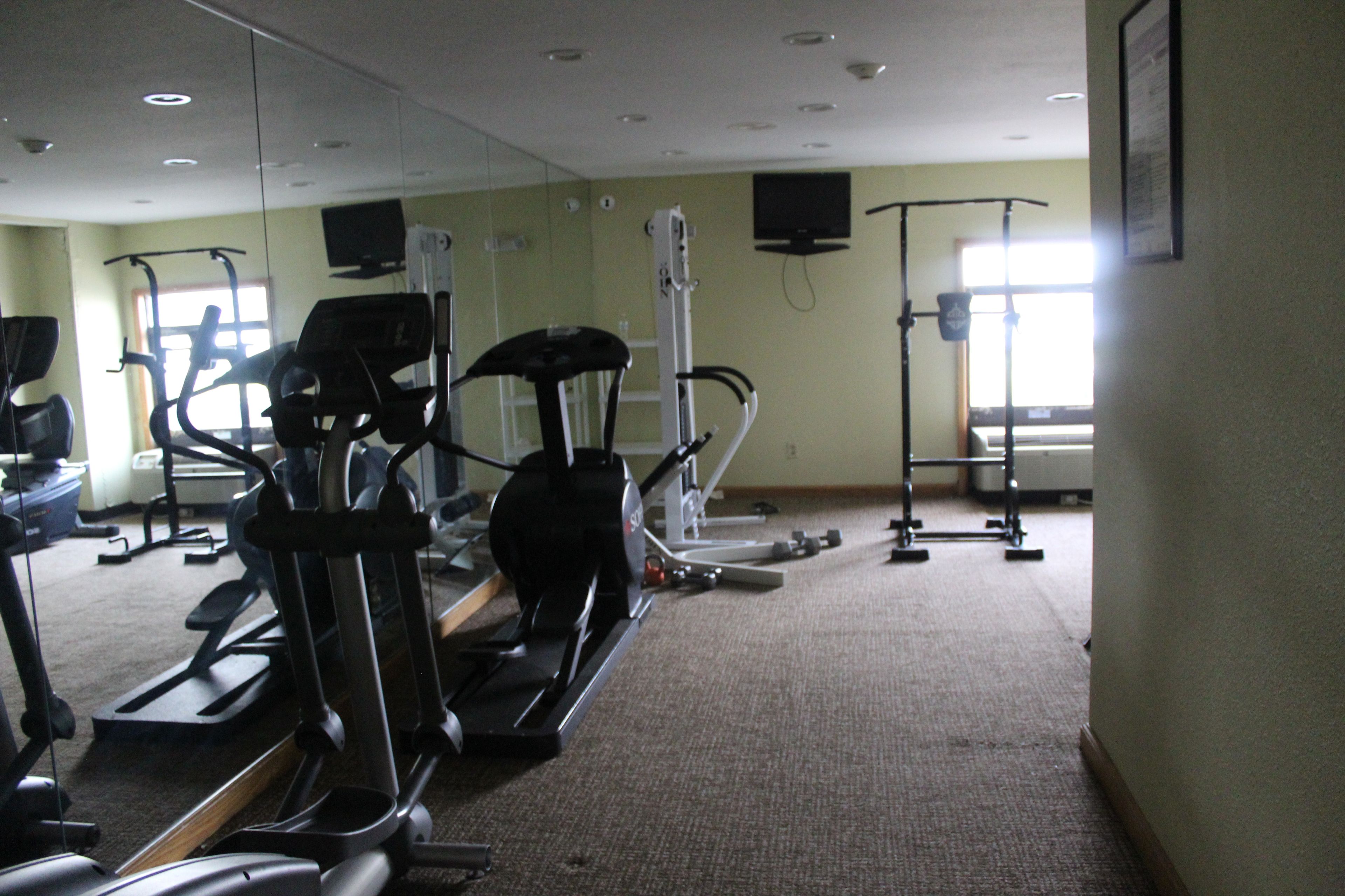 A gym with various exercise machines, a large mirror, and a television on the wall.