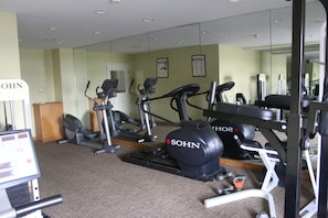 Un gimnasio con varios equipos de ejercicio, incluyendo cintas de correr y una bicicleta estática, además de un espejo de pared.