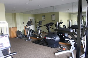 Un gimnasio con varios equipos de ejercicio, incluyendo cintas de correr y una bicicleta estática, además de un espejo de pared.