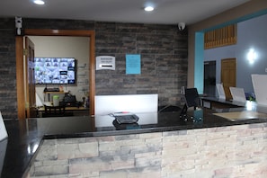 A reception desk with a stone wall, a digital display, and a sign indicating the manager is on duty. - Empire inn and Suites (Muncie)
