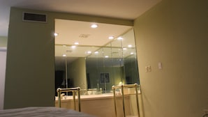 Habitación de hotel con un espejo grande, una cama, un ventanal y un baño con separador de vidrio.