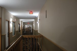 Un pasillo de hotel con piso alfombrado, barandas de madera y una señal de salida en el techo.