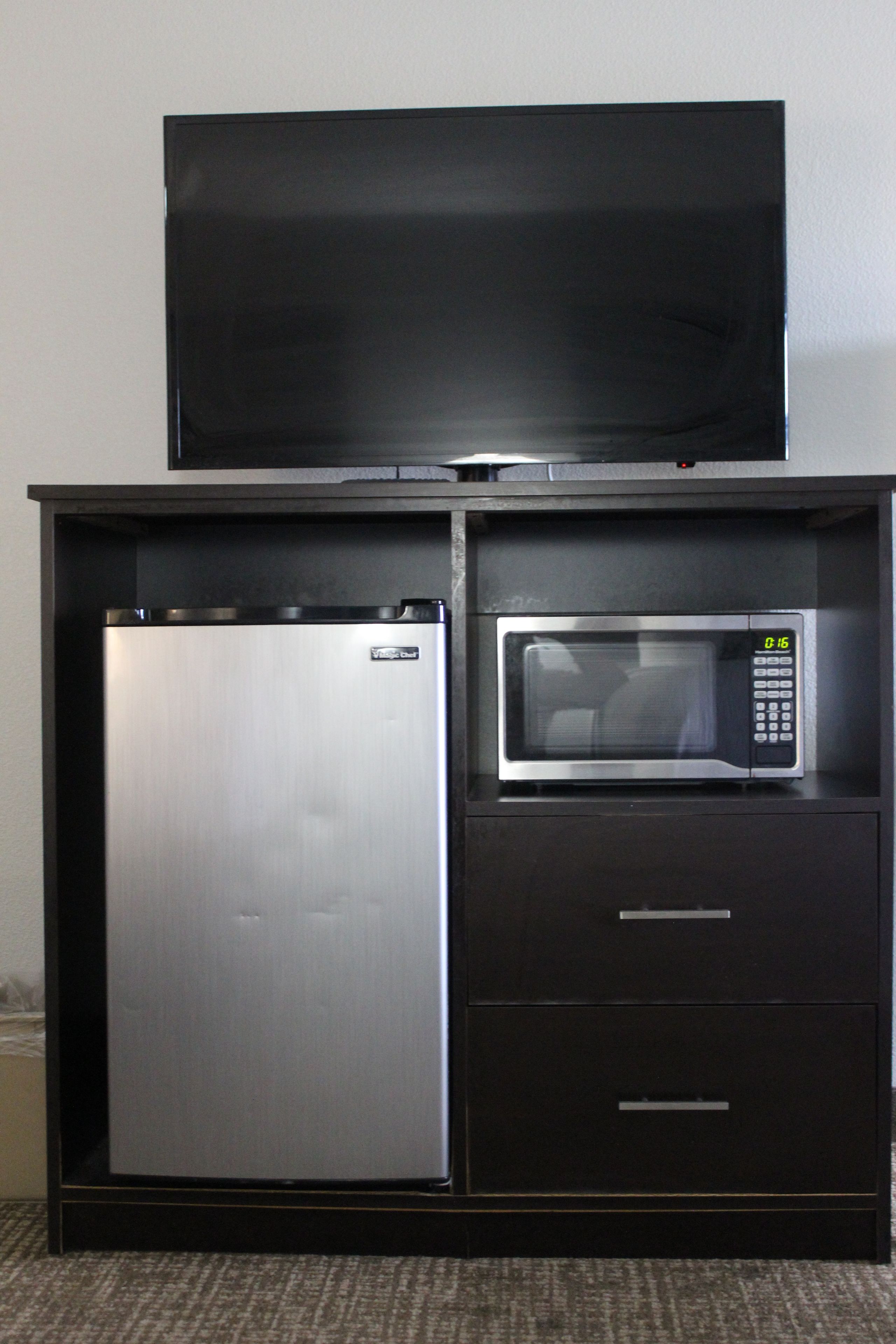 Eine kleine Küchenzeile mit Kühlschrank, Mikrowelle und einem Flachbildfernseher.