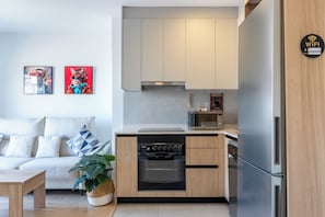 Eine moderne Küche mit Einbauofen, Mikrowelle und Kühlschrank. Im Wohnbereich befindet sich ein weißes Sofa mit gemusterten Kissen und ein Blumentopf.
