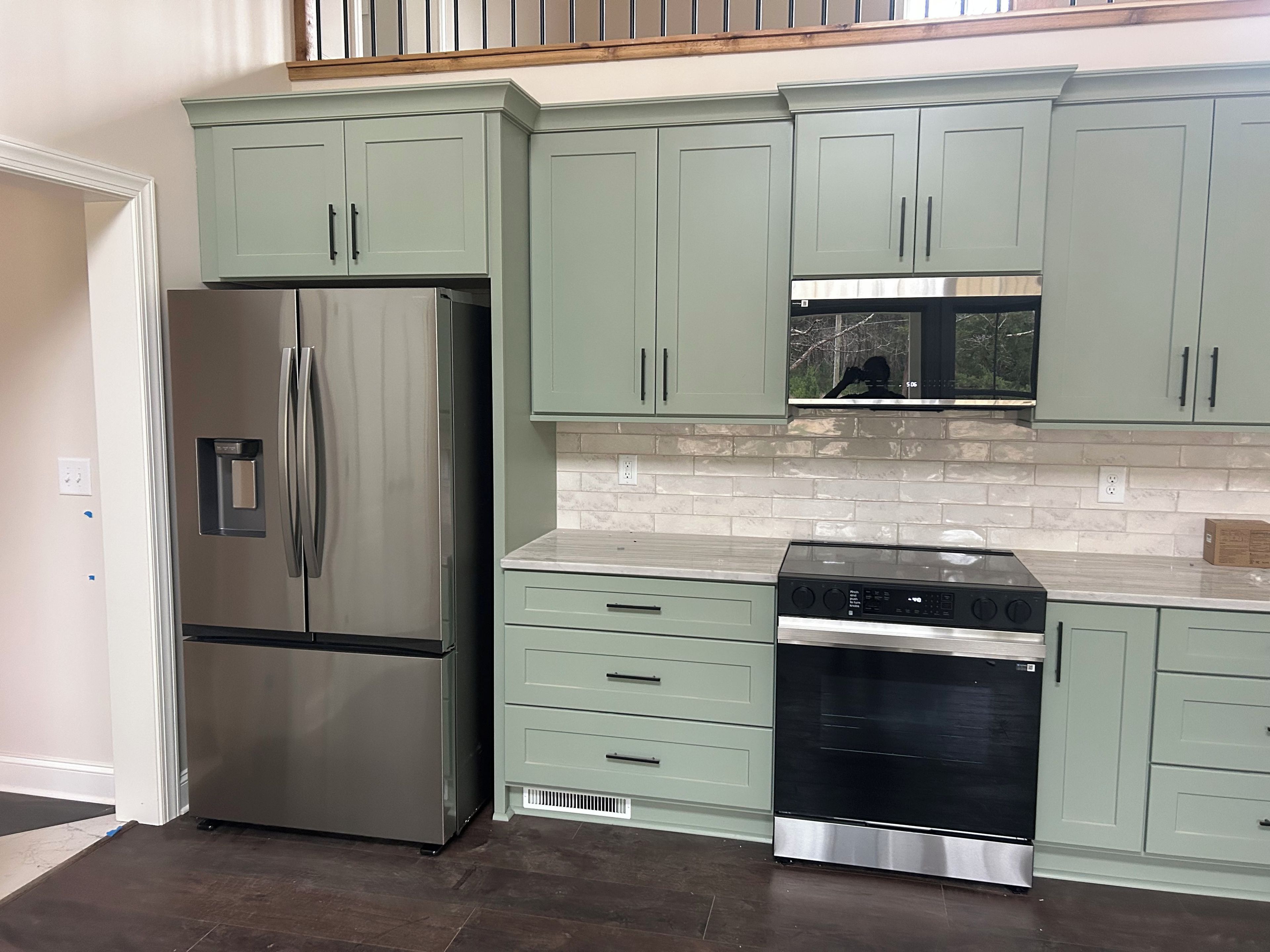 Una cocina con alacenas verde claro, un refrigerador de acero inoxidable, una estufa negra y un salpicadero de azulejos blancos.