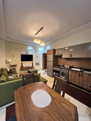A modern kitchen with built-in appliances, a dining area with a wooden table, and a living room with a green sofa. - Superb 2-bedroom apartment with AC in vibrant Rabat Agdal (Rabat)