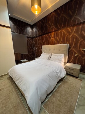 A bedroom with a large bed, a nightstand, a lamp, and a wall with a textured pattern. - Superb 2-bedroom apartment with AC in vibrant Rabat Agdal (Rabat)
