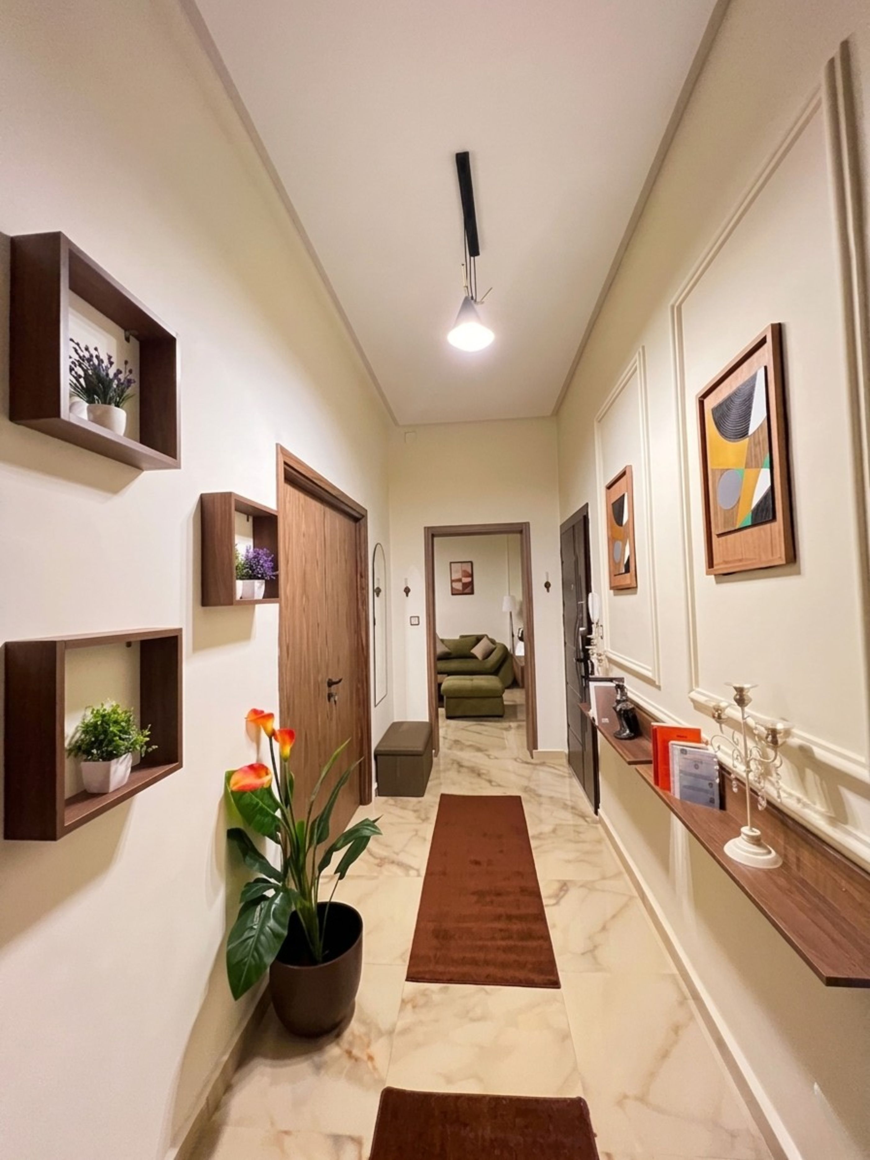A hallway with a marble floor, wooden door, and a potted plant.