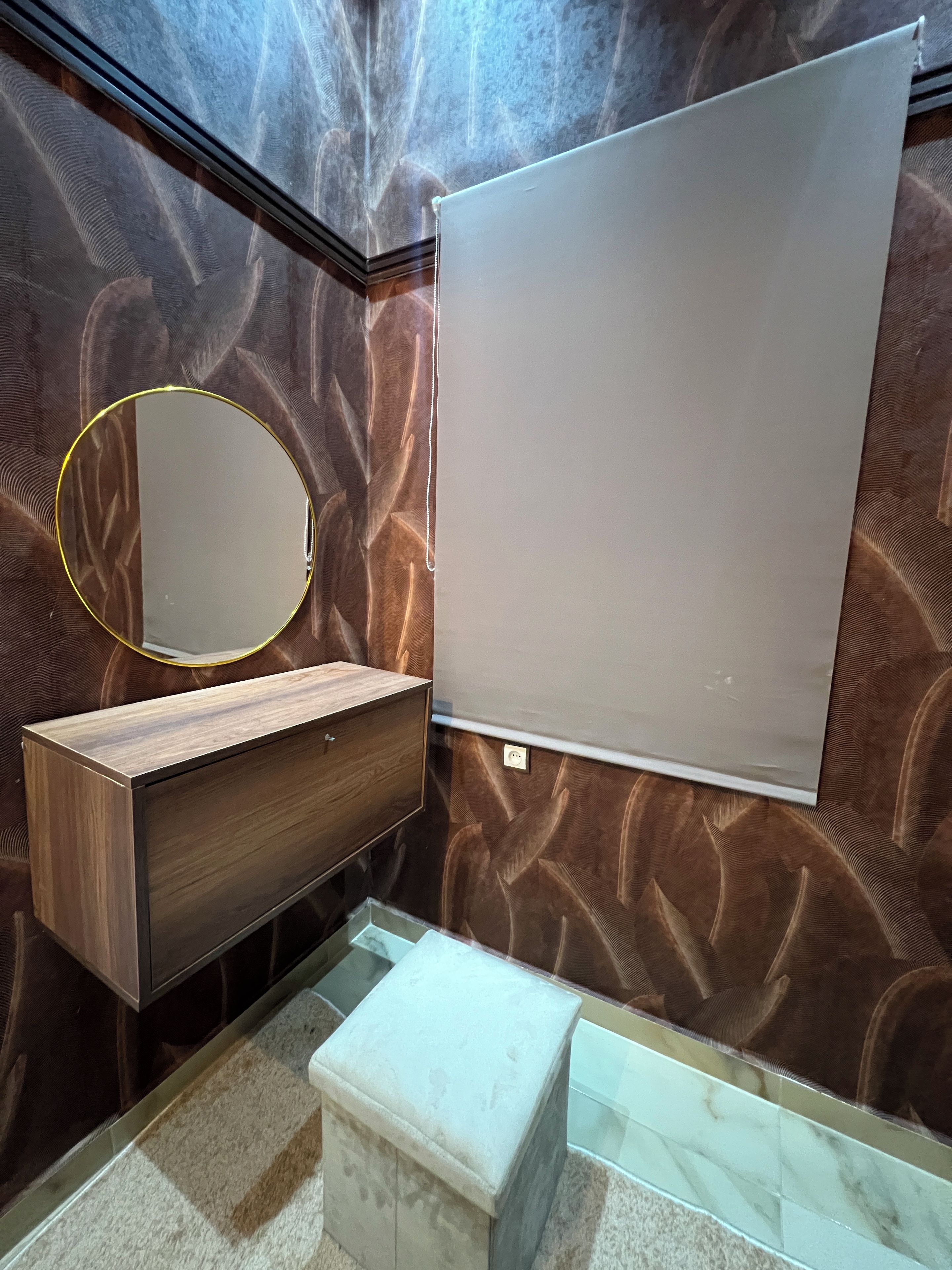 A bathroom with a wooden vanity, a round mirror with a gold frame, and a white sink.