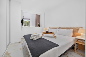 A hotel room with a bed, a window with curtains, a bedside table with a lamp, and a small tray with a teapot. - Azahara Playa Suites (Los Cristianos)