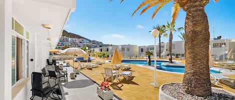 Une terrasse d’hôtel avec une piscine, des chaises longues et un palmier.