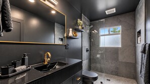 Ein modernes Badezimmer mit einem schwarzen Waschtisch, einem Goldarmaturen-Wasserhahn und einer Duschkabine aus Glas.