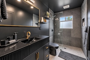 A modern bathroom with a black vanity, gold faucet, and a glass shower enclosure. - Octopus Palace (Crescent)
