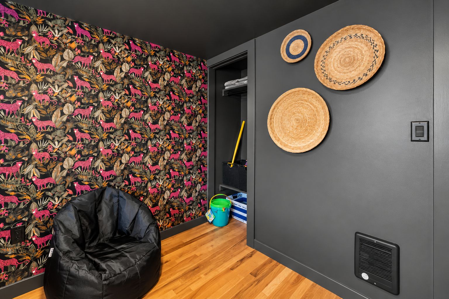 A room with a patterned wallpaper, a black bean bag chair, and two woven wall hangings.