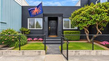 A building with a black door, a blue flag with an octopus, and a well-maintained front yard with hedges and flowers.