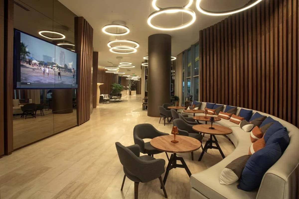 A modern lounge area with a large flat-screen TV, round tables, and a curved sofa with cushions.
