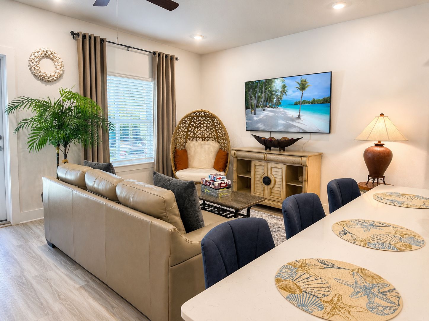 A modern living room with a sofa, dining table, chairs, a decorative lamp, a television, and a large window with curtains.